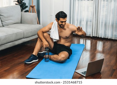 Athletic and sporty man resting on fitness mat during online body workout exercise session for fit physique and healthy sport lifestyle at home. Gaiety home exercise workout training concept. - Powered by Shutterstock