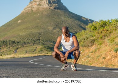 Athletic, sporty, muscular, healthy black male kneeling after losing a race along a road outdoors with a mountain background - Powered by Shutterstock