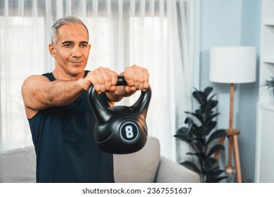 Athletic and sporty senior man engaging in body workout routine with lifting kettlebell at home as concept of healthy fit body with body weight lifestyle after retirement. Clout