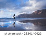 An athletic surfer man walks the beach with a surfboard. Sport travel destinaiton. Surfing lifestyle. Famara beach, Lanzarote, Canary Islands, Spain