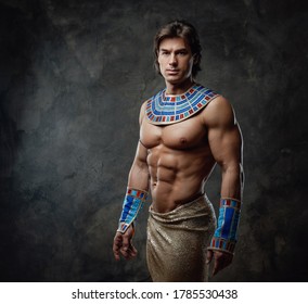 Athletic and very sexy man in representative egyptian costume posing in the studio with dark walls