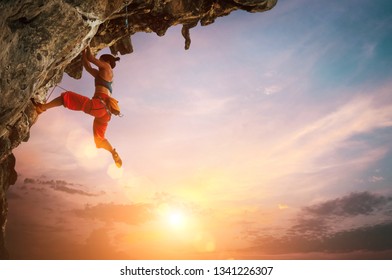 Athletic Woman climbing on overhanging cliff rock with colorful sunset sky background