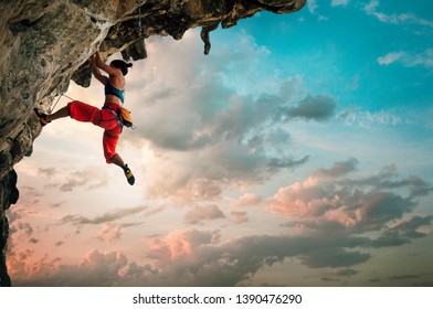 Athletic Woman climbing on overhanging cliff rock with sunrise sky background