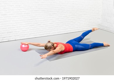 Athletic woman does pilates workout using small ball in loft fitness studio indoor. Swimming drill, front view.