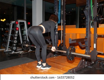 Athletic Woman Doing Dead Lift Exercise With Barbell In Gym, Back View