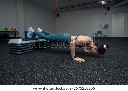 Athletic woman doing elevated push ups, targeting core strength while training intensely in sleek fitness center, demonstrating commitment to personal wellness