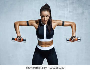 Athletic Woman Doing Exercise For Arms. Photo Of Muscular Fitness Model Working Out With Dumbbells On Grey Background. Strength And Motivation