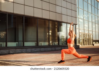 Athletic woman is doing lunge outdoors in the city, working out next to urban building.