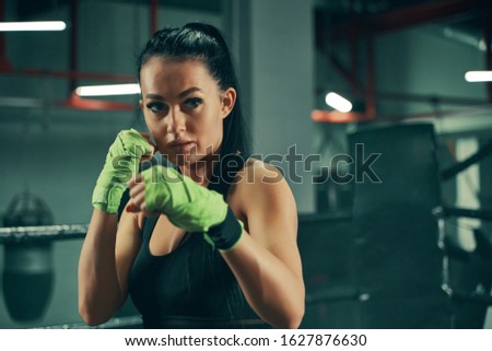Athletic woman during fighting training on boxing ring wearing green bandages on hands