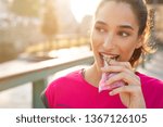 Athletic woman eating a protein bar. Closeup face of young sporty woman resting while biting a nutritive bar. Fitness beautiful woman eating a energy snack outdoor.