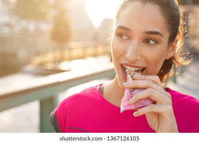 Athletic woman eating a protein bar. Closeup face of young sporty woman resting while biting a nutritive bar. Fitness beautiful woman eating a energy snack outdoor. - Shutterstock ID 1367126105