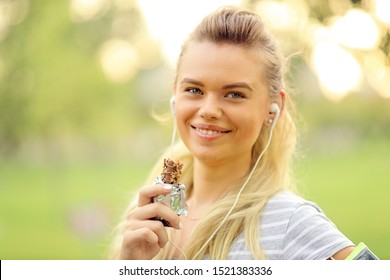 Athletic Woman Eating A Protein Bar - Closeup Portrait Of Smiling Young Sporty Girl Posing While Resting And Grabbing A Nutritive Bar