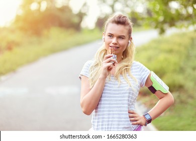 Athletic Woman Eating A Protein Bar After Running In Park - Closeup Face Of Young Sporty Girl Resting While Biting A Nutritive Bar - Fitness Beautiful Female Eating Energy Snack Outdoor.