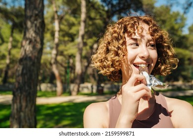 Athletic woman eating a protein bar. Fitness beautiful woman eating a energy snack outdoor. Copy space. Healthy food, outdoor sports concepts.