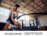 Athletic woman exercising strength with battle ropes during gym workout.