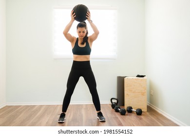 Athletic Woman In Her 30s With Strong Arms And A Toned Body Throwing A Medicine Ball During Her Functional Training At Home