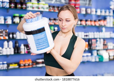 Athletic Woman Holding Plastic Jar With Sport Nutrition, Reading Label Carefully Before Buying In Shop