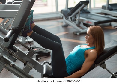 Athletic Woman Lifting Weight In Gym. Leg Press.