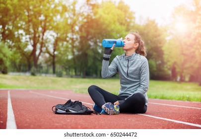 Athletic woman on running track drinking water during training, sport fitness accessories - Powered by Shutterstock