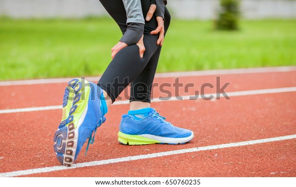 Athletic woman on running track has calf cramp\
and touching hurt leg during\
workout