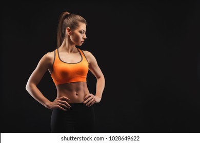 Athletic woman posing in studio, bodybuilder. Muscular body and strong muscles. Shot on black background, low key. Bodybuilding concept, copy space