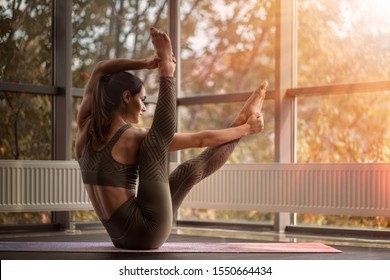 Athletic woman practices yoga. Sun shines through the window