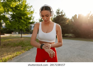 Athletic woman preparing for exercise using smartwatch while listening to music through wireless headphones outdoors