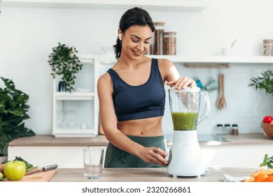 Athletic woman preparing smothie while listening music with earphones in the kitchen at home. - Powered by Shutterstock