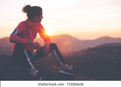 Athletic woman resting after a hard training in the mountains at sunset. Sport tight clothes. 
