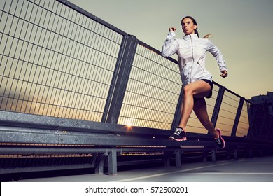Athletic woman running during sunset on rooftop of parking, garage - Shutterstock ID 572500201