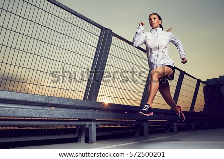 Athletic woman running during sunset on rooftop of parking, garage