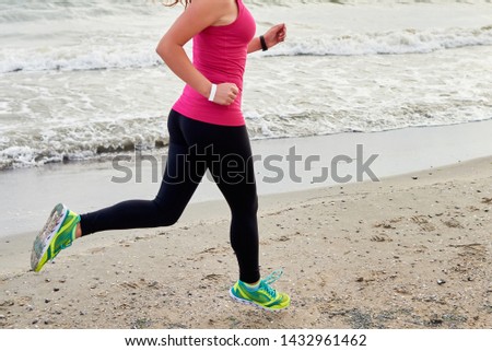 Athletic woman running on ocean beach, copy space. Female runner working out at summer morning, side view. Unrecognizable body jogging. Healthy lifestyle concept