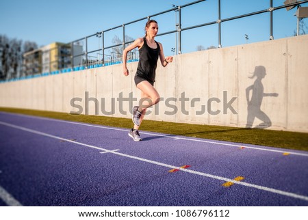 Athletic woman running on stadium track during sunny day