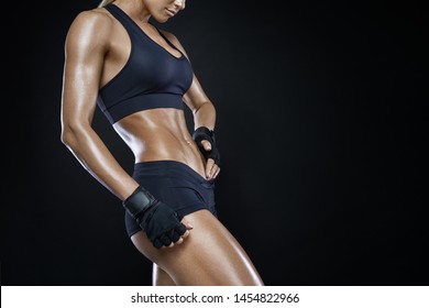 Athletic woman with strong abdominal muscles posing with her hands on her hips with copy space. Attractive muscular woman with gloved hands on strong abs. Muscular pumped woman after workout.