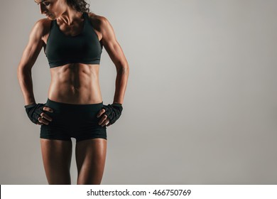 Athletic Woman With Strong Abdominal Muscles Posing With Her Hands On Her Hips In Shadowed Light To Emphasise Her Physique, With Copy Space