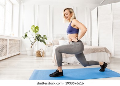 Athletic woman in stylish sportswear doing lunges exercises at home in bedroom. Attractive blonde-hair girl standing on blue mat, working out to keep fit, healthy lifestyle concept