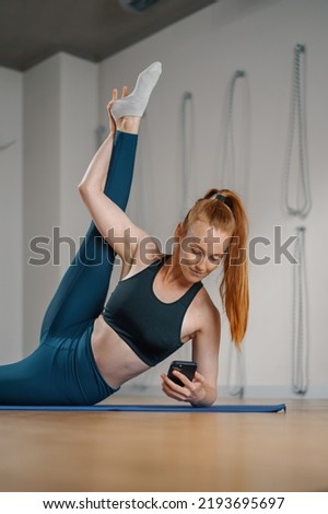Athletic woman texting on the phone while doing stretching pilates yoga for health in studio. athletic body girl