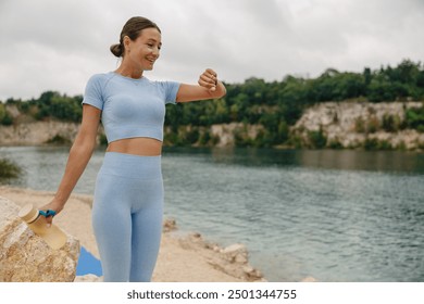 An Athletic Woman Thoughtfully Checking Her Watch by a Gorgeous Scenic Water Body Outdoors - Powered by Shutterstock