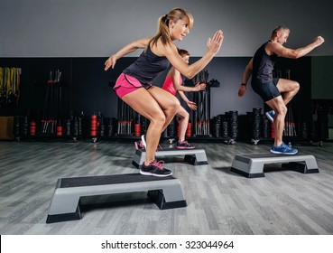 Athletic woman trainer doing aerobic class with steppers to people group on a fitness center. Sport and health concept.