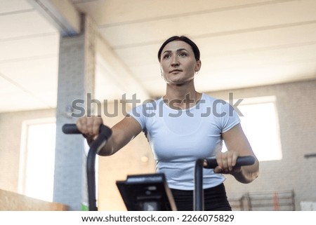 Athletic woman training on assault bike in crossfit gym.