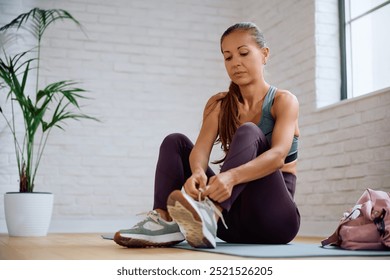 Athletic woman tying shoelace on her sneakers in health club. Copy space. - Powered by Shutterstock