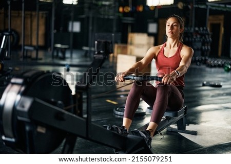 Athletic woman using rowing machine during cross training in a gym.