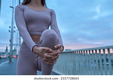 An athletic woman warming up with stretching legs on an urban bridge. Focus on a knee                               - Powered by Shutterstock