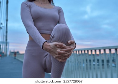 An athletic woman warming up with stretching legs on an urban bridge. Focus on a knee                               - Powered by Shutterstock