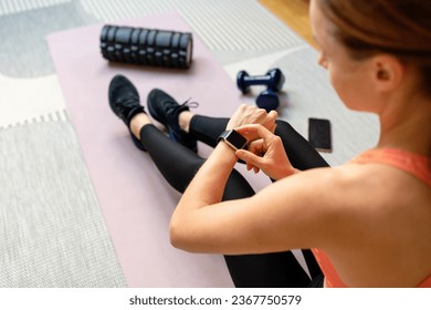 Athletic woman wearing sportswear woman sits on exercise mat and launching training program on her smart watch. Fitness and personal digital devices. - Powered by Shutterstock