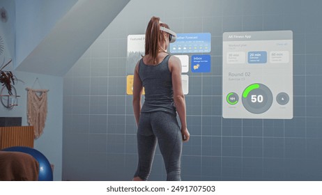 Athletic woman wearing VR headset starts online training. VR screen with displayed virtual coach and interface of fitness app with workout plan. Metaverse futuristic home gym with AI technologies. - Powered by Shutterstock