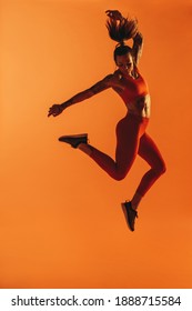 Athletic woman working out on orange background. Monochrome fitness portrait of female athlete doing jumps.