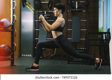 Athletic woman workout out squats weighted lunges exercise with suspension straps in fitness club or gym