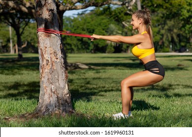 Athletic Woman Workout Squats With Resistance Band Outdoors. Fitness Girl Doing Exercise For Back And Legs At The Park