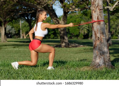 Athletic Woman Workout Squats With Resistance Band Outdoors. Fitness Girl Doing Exercise For Back And Legs At The Park